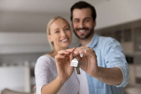 Close up focus of happy young Caucasian couple show keys to first share own apartment or house. Smiling millennial man and woman celebrate relocation to new home. Moving, rental, estate concept.の写真素材