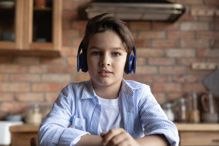 Close up screen view of small Caucasian boy child in headphones talk speak on video call at home. Headshot portrait of little kid in earphones study distant have webcam virtual lesson on computer.の写真素材