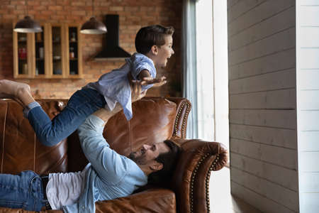 Caring young Caucasian father have fun play with excited little 7s son on family weekend at home. Happy dad hold small child fly up in air feel playful together in living room. Entertainment concept.の写真素材
