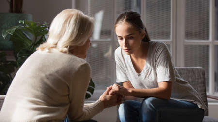 Supportive older Caucasian mom hold hands comfort caress talk with millennial female child feeling unhappy sad. Loving senior mother show support and care to upset depressed adult grownup daughter.の写真素材
