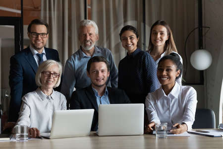 Portrait of smiling diverse multiracial employees colleagues work together on computers in shared workplace. Happy multiethnic businesspeople brainstorm cooperate on laptops in office.の写真素材