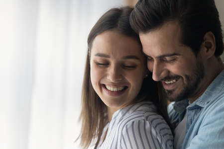 Close up smiling woman and man, young couple enjoying tender moment, hugging, standing at home, happy wife and husband expressing love and care, spending free time together, romantic date conceptの写真素材
