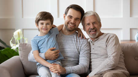 Portrait of three generations of Caucasian men sit relax on cozy couch in living room at home...