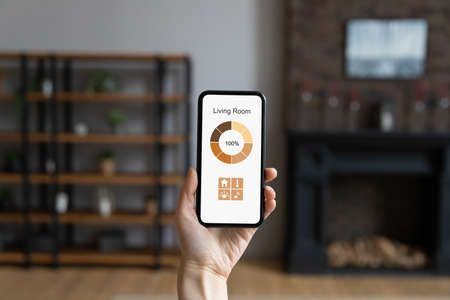 By single touch. Close up cropped shot of phone with smart home control app on screen in woman hand....