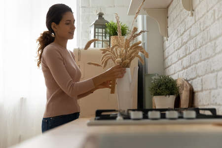 Bringing comfort coziness to kitchen. Young latin female homeowner first time buyer enjoy decorating...
