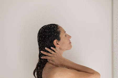 Side view beautiful woman standing under water drops in bathroom, washing hair, attractive young...