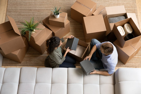 Top view happy couple unpacking boxes with belongings together, sitting on floor, moving day, wife...