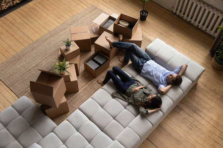 Top view happy couple tenants homeowners relaxing on couch on moving day in living room with...