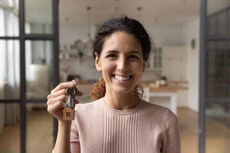 Happy excited millennial latina woman buying modern studio apartment first time look at camera pose indoors hold key in hand. Portrait of overjoyed lucky young lady win new flat as top lottery prizeの写真素材