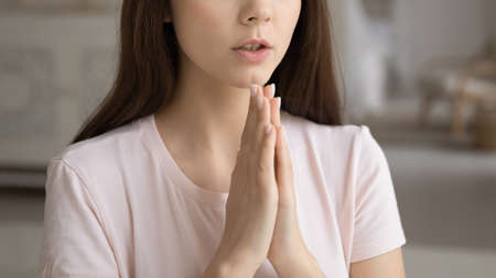 Faithful young woman keeping hands together in pray to god. Cropped shot of religious teen girl,...