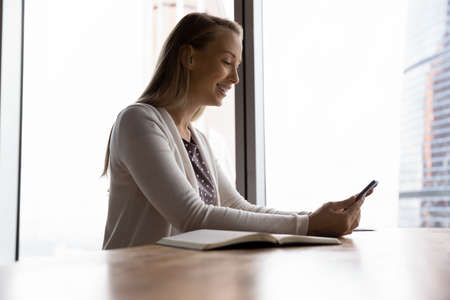 Smiling millennial female sit at desk talk speak on video call online on smartphone. Happy Caucasian...