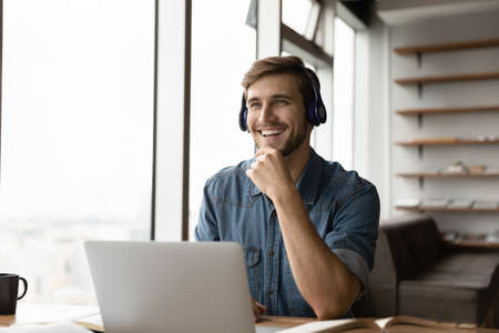 Overjoyed millennial Caucasian male employee in headphones work online on laptop talk with colleague coworker. Smiling young man in earphones have webcam zoom video call. Virtual event concept.の写真素材