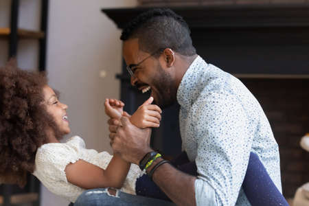 Happy dad and excited laughing daughter girl enjoying funny fight at home. Daddy cuddling and tickling cute kid, relaxing, playing active games with child at home. Family, being father conceptの写真素材