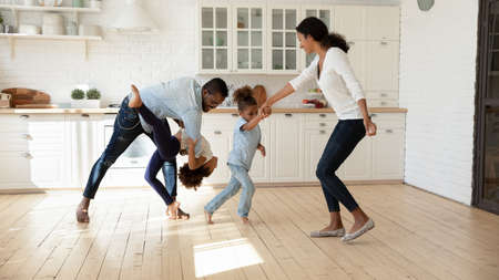 Excited African American family celebrating moving into new house. Happy parents and kids dancing in big modern kitchen interior, playing active games, exercising, having fun together at home partyの写真素材