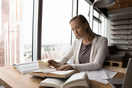 Smart teen female student sit at desk at home handwrite study with books prepare for exam. Focused...