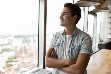 Happy young male employee look in window distance thinking or planning career perspectives...