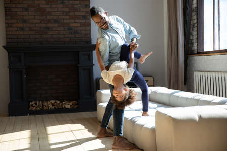 Happy dad and teaching excited little daughter to dance rock-n-roll. Daddy and kid having fun and enjoying leisure at home party, playing active energetic games and exercising in living roomの写真素材