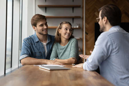 Happy couple clients talk speak with male relator or broker at office meeting, plan buying home together. Smiling Caucasian man and woman have consultation with real estate agent. Rental concept.の写真素材