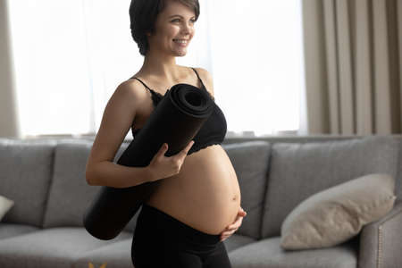 Smiling Caucasian pregnant woman in sportswear ready for morning gymnastics or exercise. Happy young female follow healthy lifestyle during pregnancy, hold yoga mat for Pilates or stretching.の写真素材