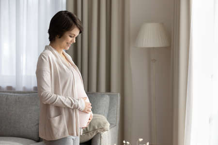 Smiling young Caucasian woman touch caress baby bump enjoy easy healthy last month of pregnancy....