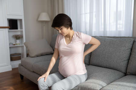 Unhealthy young pregnant woman suffer from lower back pain on last month of pregnancy. Unwell tired female have spinal painful feeling or ache from baby bump weight. Maternity, health problem concept.の写真素材