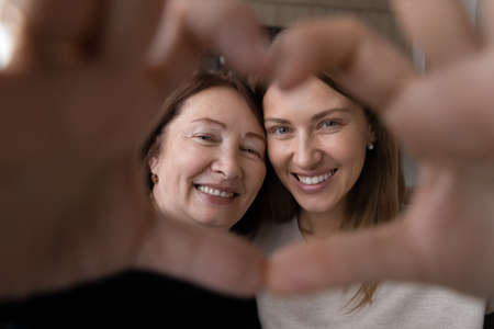 Portrait of happy elderly Caucasian mother and adult daughter make heart love hand gesture or sign...