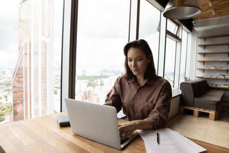 Smiling young Caucasian businesswoman sit in modern company office building consult clients online...