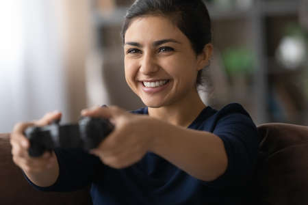 Close up happy Indian woman playing video game on tv, having fun, holding controller, sitting on couch at home, excited interested young female enjoying leisure time, involved in funny virtual appの写真素材