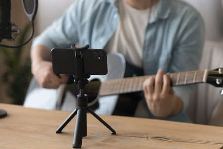 Close up smartphone on tripod, cropped of man playing guitar, musician artist recording new song...