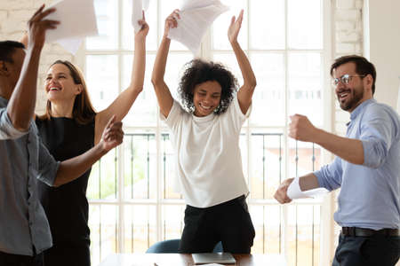 Happy young african american female team leader having fun with multiracial colleagues, dancing to...