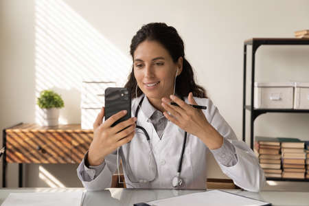 Stay healthy. Young lady doctor in wired headphones answer patient phone call from clinic office...