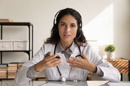 Medical conference. Latin female doctor surgeon therapist in headset look at camera talk share...