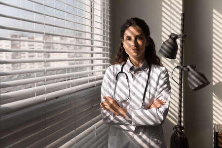 Confident doctor. Headshot portrait of young hispanic female in white lab coat professional medical...