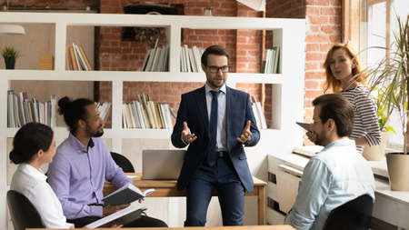 Confident businessman in suit and glasses leading briefing, business coach mentor training diverse...