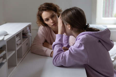 Caring mother talking to stressed unhappy adolescent daughter, helping in difficult life situation, giving advices against bullying in school or solving psychological problem, child protection conceptの写真素材