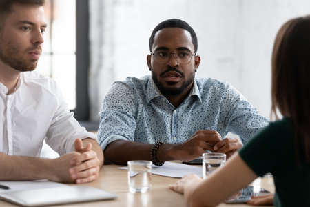 Focused African American HR manager talking to job candidate on interview. Millennial business team meeting at conference table, discussing solutions, brainstorming and working on project togetherの写真素材