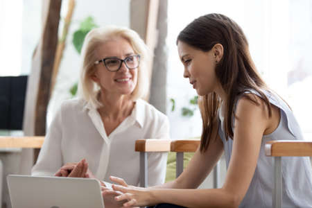 Smiling businesswomen use laptop discuss financial business online project at team office meeting. Happy female employees colleagues brainstorm work together on computer at briefing. Teamwork concept.の写真素材