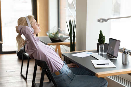 Calm businesswoman in headphones relaxing, peaceful employee or student leaning back in chair, sitting at work desk with laptop and resting after work done, enjoying break, listening to musicの写真素材