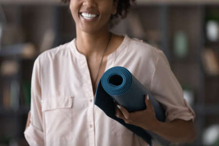 Close up sincere smiling young african ethnicity mixed race woman holding yoga mat in hands, feeling excited of starting yoga pilates class improving body, healthy lifestyle mindfulness concept.の写真素材
