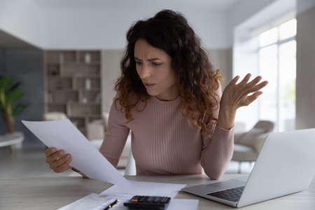 Unhappy young Latino woman manage family budget finances feel distressed with bad news in paperwork letter or correspondence. Hispanic female pay bills online frustrated by debt or bankruptcy notice.の写真素材