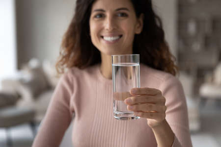 Close up portrait of smiling millennial Hispanic woman recommend drinking clean still mineral water for body refreshment. Happy young Latino female enjoy pure clear aqua. Hydration, habit concept.の写真素材
