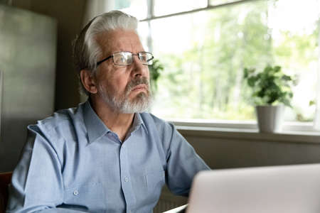 Pensive old Caucasian man distracted from computer work look in distance thinking pondering of...