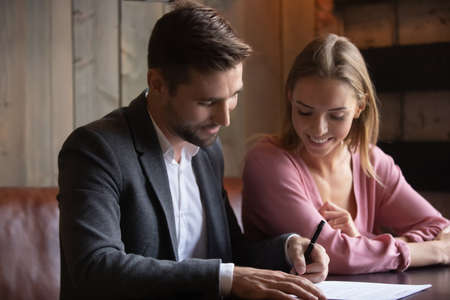 Happy beautiful young caucasian family couple signing paper contract at meeting in modern cafe....