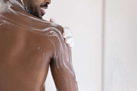 Muscular back of mixed race African bearded guy, taking shower, applying foamy gel or soap on smooth dark skin. Male morning bath routine, daily hygiene, bodycare concept. Cropped shot, close upの写真素材
