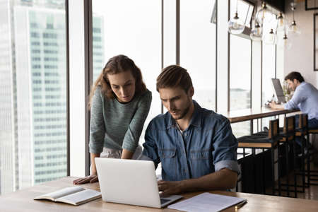Concentrated young business lady helping male colleague with online computer project, working...