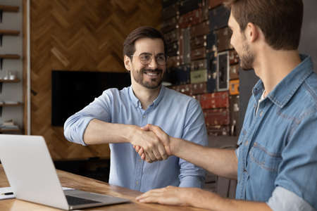 Smiling young male hr manager boss leader shaking hands with job candidate, feeling satisfied with...