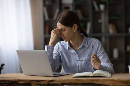 Overwhelmed unhappy young business woman employee worker taking off eyeglasses, feeling stressed due...