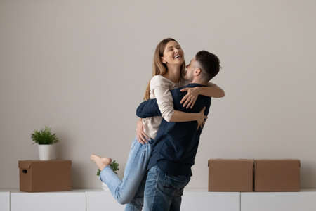 Smiling young man and woman hug relax on moving day buying first shared house together. Happy...
