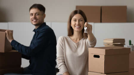 Portrait of smiling young Caucasian couple hold keys to new house unpack on moving relocation day...