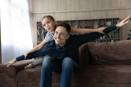 Overjoyed young Caucasian dad feel playful with little teenage daughter involved in funny game relax rest together at home. Smiling father play with happy teen girl child. Entertainment concept.の写真素材